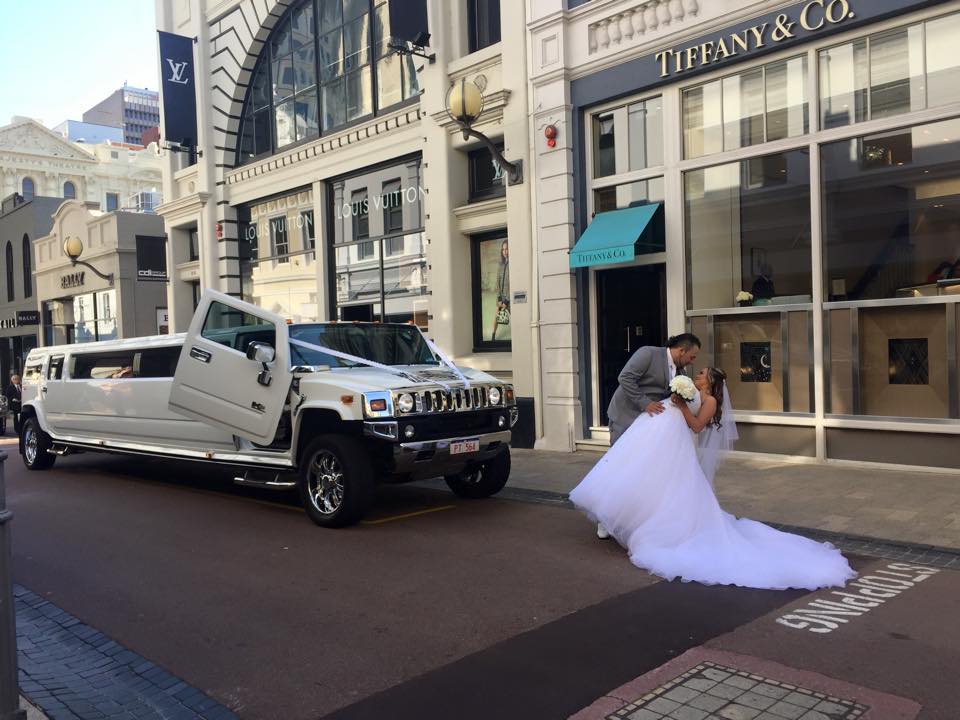 Bride and groom kissing in front of a brand new custom Hummer wedding limo
