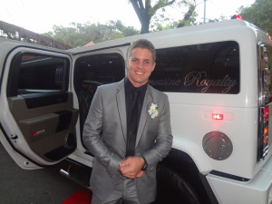 Johnny Ruffo in grey fitted suit posing with Limousine Royalty Hummer limo