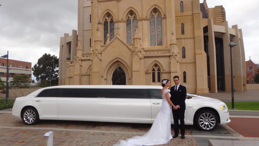 Bride and groom outside church with wedding limousine